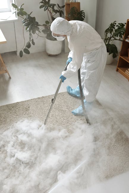 A professional cleaner from Shoreditch Carpet Cleaners is performing deep cleaning in a modern conference room. The individual, dressed in a beige jumpsuit, is bent over using a yellow industrial carp